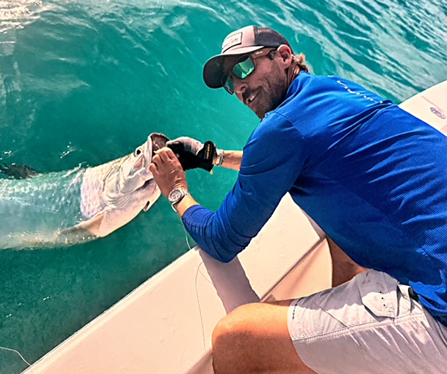 Angler in a blue shirt holding a tarpon by the jaw for release