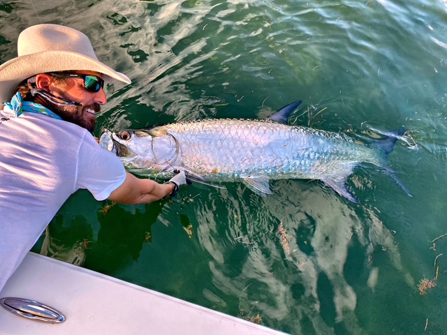 Angler in a wide brim hat holding a tarpon boatside in Key West
